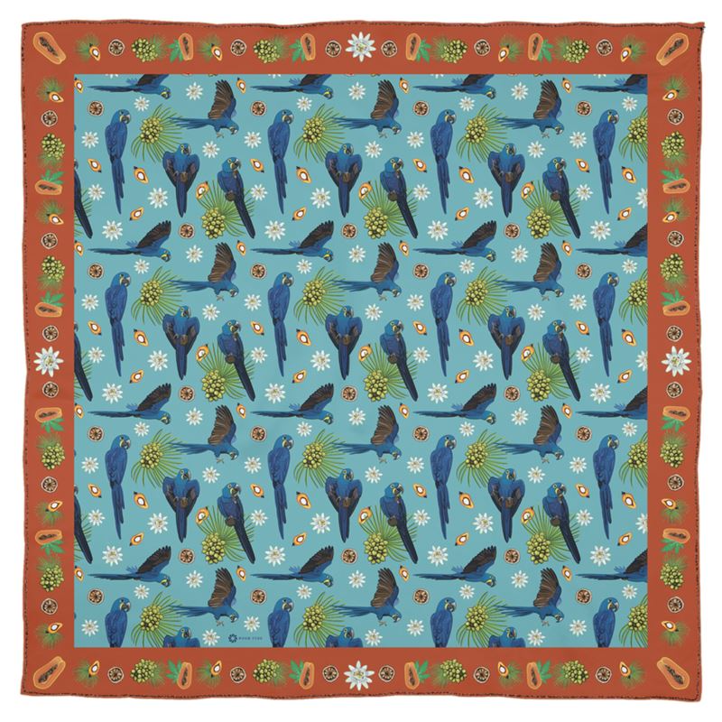 The hyacinth macaw is sometimes called the gentile giant of parrots, even though it the largest parrot of South America and can easily crack a coconut in its beak! This lovely square Georgette silk scarf honors this remarkable parrot with vibrant blue feathers and the delicate ecosystem of fruits and nuts it loves to feed on. The Orange border is decorated with palm and Brazil nuts, papayas, and flowers. While the lush blue center square shows the parrots flying through flowers and palm fronds.