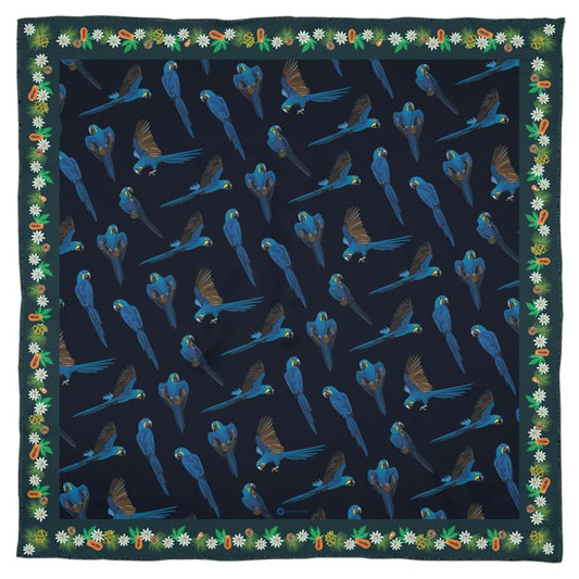 The hyacinth macaw is sometimes called the gentile giant of parrots, even though it the largest parrot of South America and can easily crack a coconut in its beak! This lovely square Georgette silk scarf honors this remarkable parrot with vibrant blue feathers, and the delicate ecosystem of fruits and nuts it loves to feed on. The deep green border is decorated with palm and Brazil nuts, papayas, and flowers. While the lush dark blue center square shows many parrots flying.