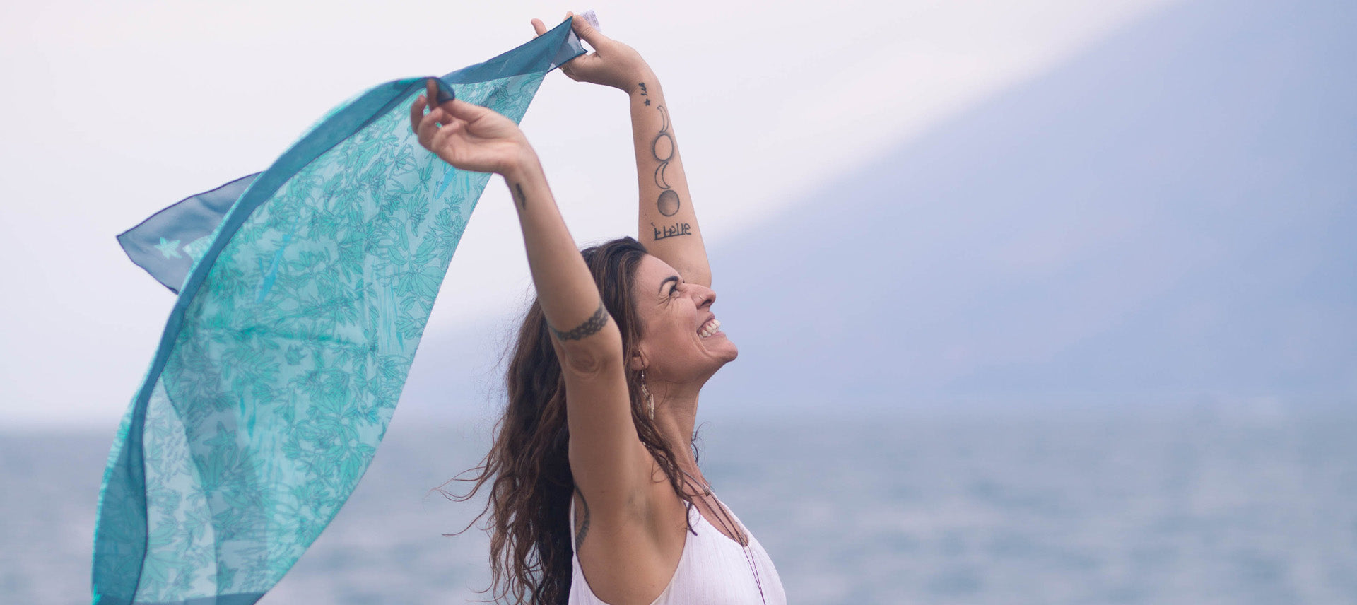 Woman with silk scarf blowing in the wind. Scarf is printed in blues with illustrated images of the mangrove ecosystem.