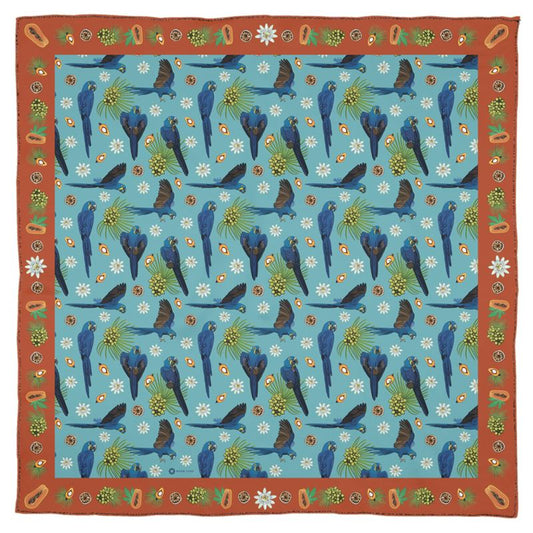 The hyacinth macaw is sometimes called the gentile giant of parrots, even though it the largest parrot of South America and can easily crack a coconut in its beak! This lovely square Georgette silk scarf honors this remarkable parrot with vibrant blue feathers and the delicate ecosystem of fruits and nuts it loves to feed on. The Orange border is decorated with palm and Brazil nuts, papayas, and flowers. While the lush blue center square shows the parrots flying through flowers and palm fronds.